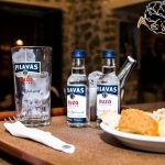 Ποτήρι με πάγο, μικρά μπουκάλια ούζου και πιάτο με μεζέ σε τραπέζι του Καϊξή