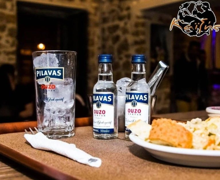 Ποτήρι με πάγο, μικρά μπουκάλια ούζου και πιάτο με μεζέ σε τραπέζι του Καϊξή