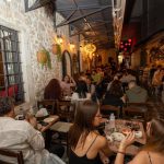 Τραπέζια με πελάτες μέσα στη στεγασμένη Στοά Μαραμένου, με πέτρινους τοίχους και φανάρια